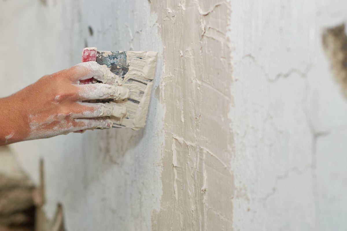 Man's hand patching wall with cement.